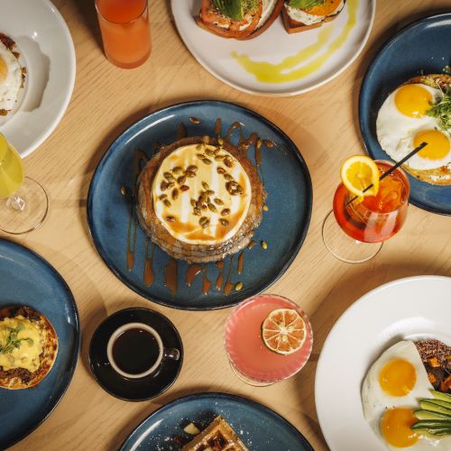 Brunch spread: sunny-side eggs on toast and roasted veggies, plus drinks of orange juice and coffee on a table.