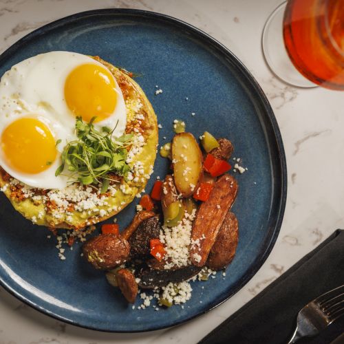 A plate of sunny-side-up eggs with crumbled cheese, plus roasted sausage and colorful vegetables.
