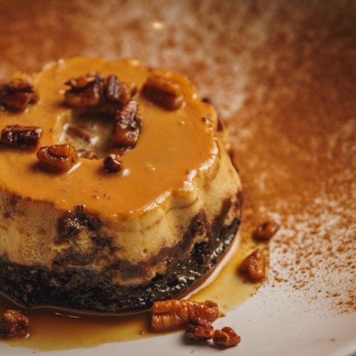 A creamy dessert/pudding topped with glossy orange sauce and caramelized nuts, served on a plate with drizzled caramel.
