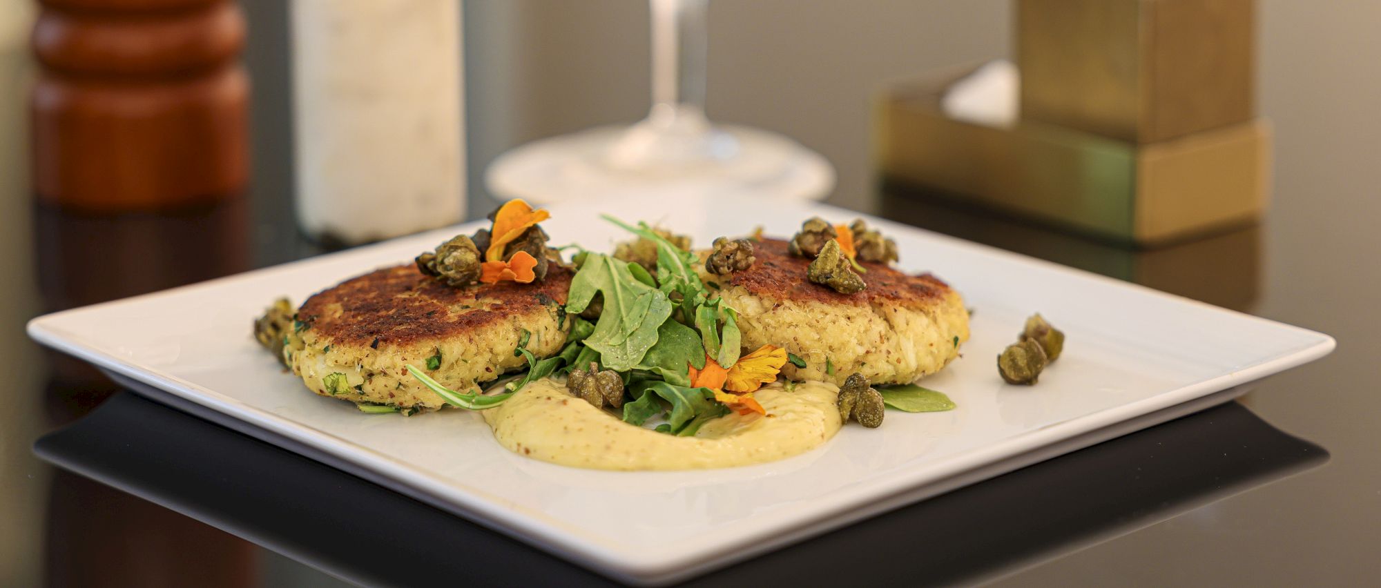 Two veggie patties atop a creamy sauce, garnished with greens, capers, and orange zest on a white plate. Delicious, plant-based comfort food.
