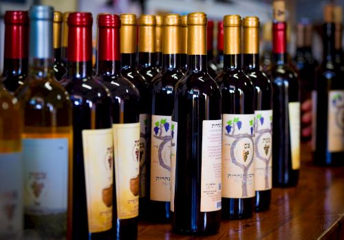 A row of wine bottles with colored caps (gold, red, black) lined up on a wooden counter.