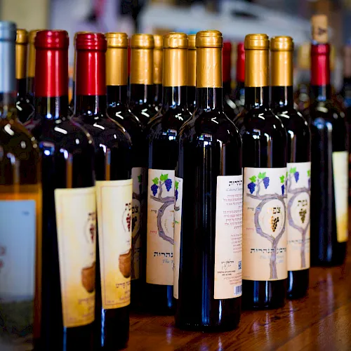 A row of wine bottles with colored caps (gold, red, black) lined up on a wooden counter.