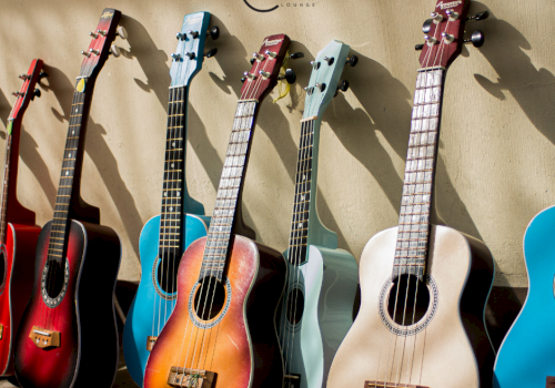 The image shows a row of colorful guitars and ukuleles leaning against a wall, with the word "CURVE" and a logo above them.