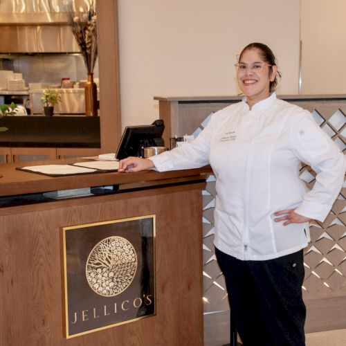 A chef in a white uniform stands at a restaurant reception desk with a 