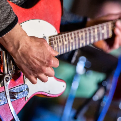 A close-up of a person playing a red electric guitar, focusing on the hands and the instrument.