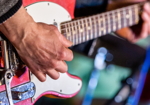 A person is playing an electric guitar, showing close-up details of their hands and the instrument.