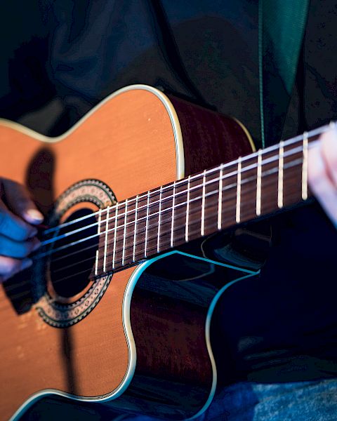 A person is playing an acoustic guitar, with their left hand on the fretboard and their right hand near the soundhole strumming or picking the strings.