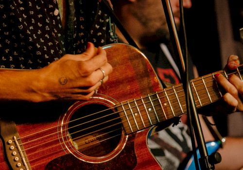A musician strums a red acoustic guitar while a microphone stand sits nearby on a stage.