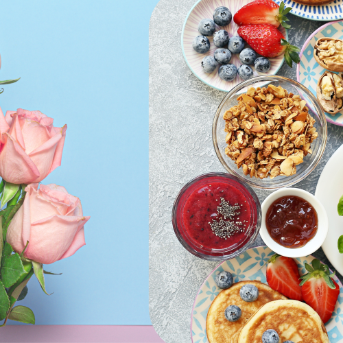 The image shows pink roses on the left and a breakfast spread on the right, featuring fruits, nuts, granola, pancakes, and a croissant with a runny egg.