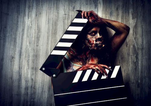 A person with zombie makeup holding a large clapperboard, standing against a textured wall, creating a dramatic horror theme.