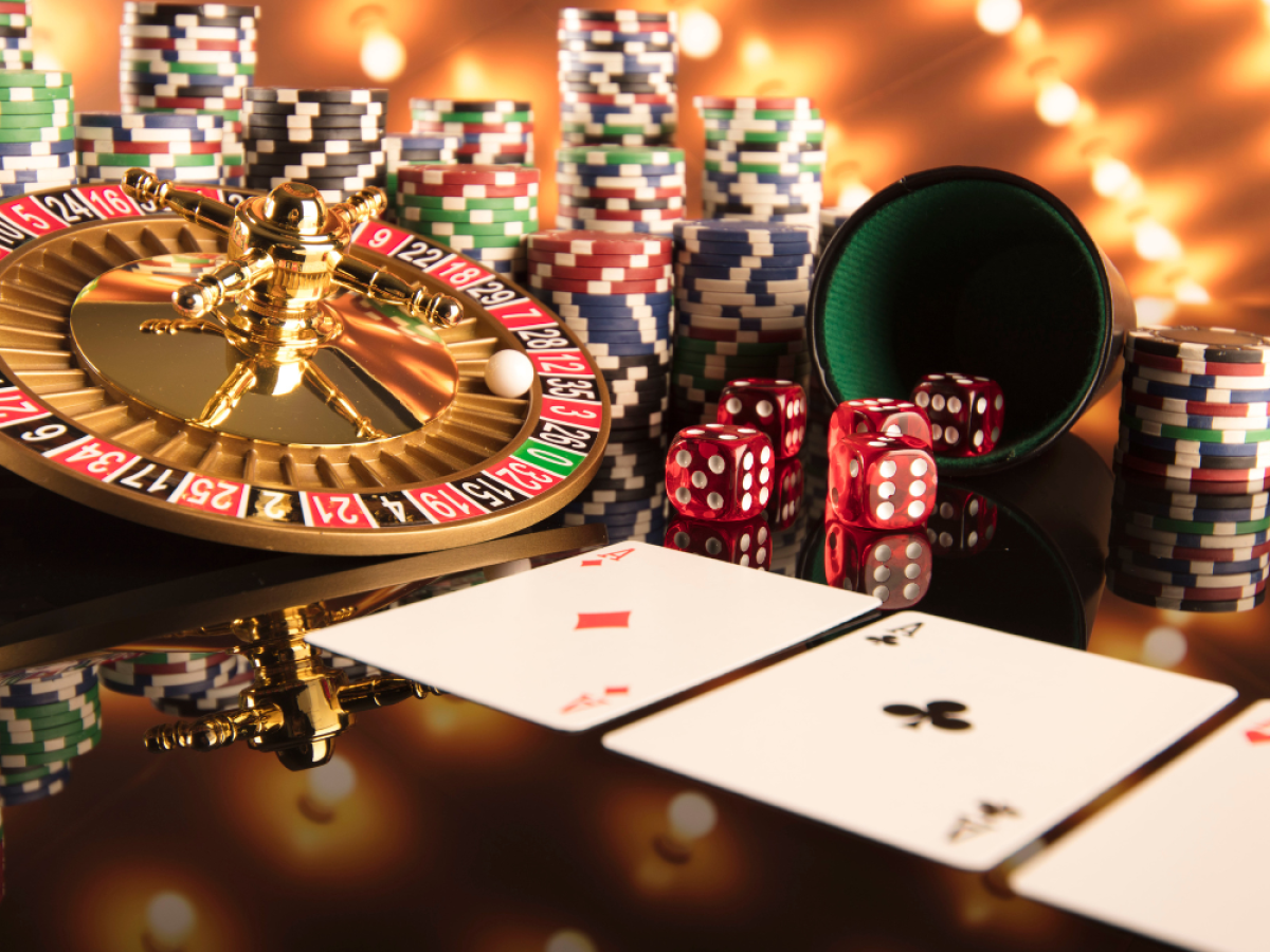 A casino scene with a roulette wheel, poker chips, playing cards, and dice on a reflective surface, surrounded by warm lights.