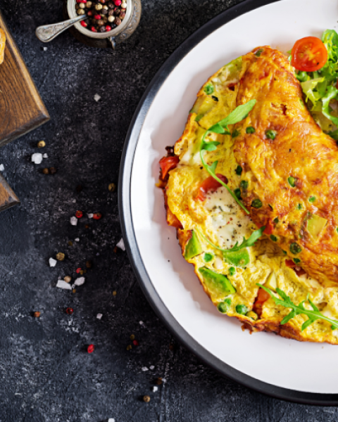 A plate with a loaded omelette, garnished with greens and tomatoes, beside some sliced bread.