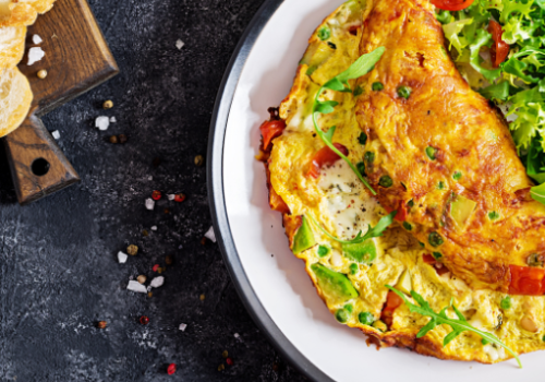 A plate with a loaded omelette, garnished with greens and tomatoes, beside some sliced bread.