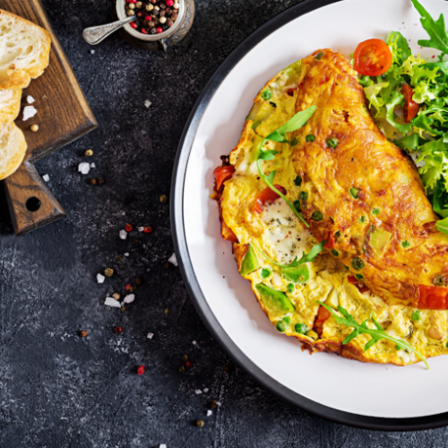 A plate with a loaded omelette, garnished with greens and tomatoes, beside some sliced bread.