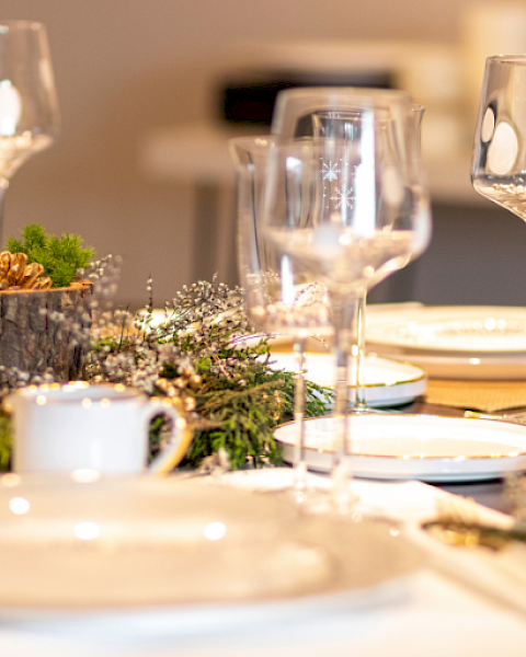 A festive dining table set with plates, glassware, and a centerpiece featuring pine cones and greenery, ready for a celebration.