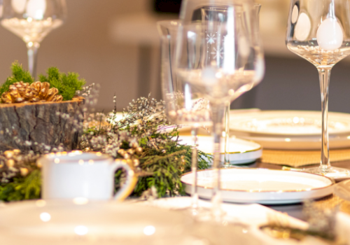 A festive dining table set with plates, glassware, and a centerpiece featuring pine cones and greenery, ready for a celebration.